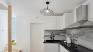 Une cuisine moderne avec des meubles blancs, un plan de travail noir et un luminaire suspendu original.