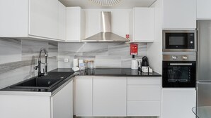 Une cuisine moderne avec des armoires blanches, un comptoir noir, une hotte de cuisinière en acier inoxydable, un four encastré, un four à micro-ondes et une machine à café.