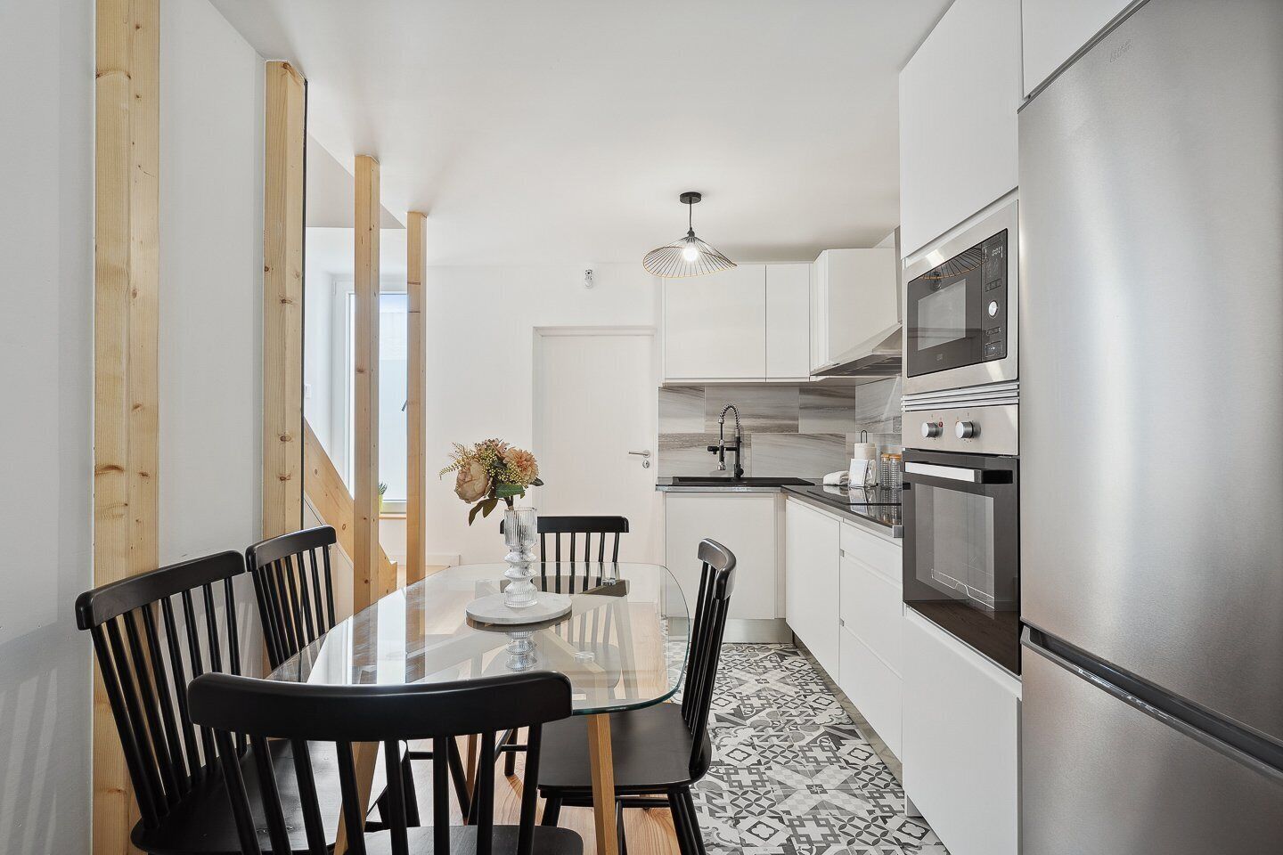 A modern kitchen with white cabinets, a stainless steel refrigerator, and a dining area with a glass table and black chairs.