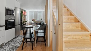 Une cuisine moderne dotée d’appareils électroménagers intégrés, un coin repas avec une table et des chaises, et un escalier en bois.