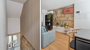 Un salon moderne avec un mur en pierre, une bibliothèque noire, un canapé bleu et un coin repas comprenant une table et des chaises.