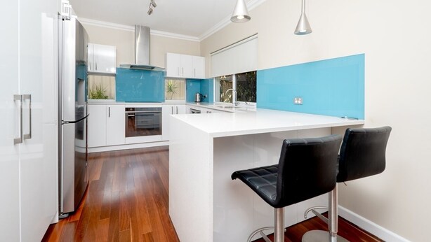 A modern kitchen with white cabinetry, a blue accent wall, and a central island with two black bar stools.