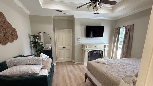 A hotel room with a bed, a sofa, a TV, a ceiling fan, and a fireplace. - Spacious 4BR Oasis with private pool perfect for families & Groups (Longview)