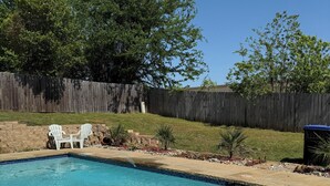 A rectangular swimming pool with clear blue water, surrounded by a stone deck. There are two white Adirondack chairs and a small trash can in the background. - Spacious 4BR Oasis with private pool perfect for families & Groups (Longview)