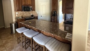 A kitchen with a granite countertop, wooden cabinets, a stainless steel microwave, a coffee maker, and a trash can. - Spacious 4BR Oasis with private pool perfect for families & Groups (Longview)