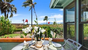 An outdoor dining area with a table set for two, surrounded by tropical plants and a view of the landscape.