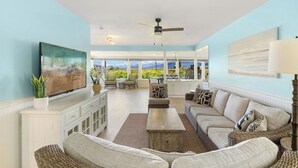 A spacious living room with a large TV, comfortable seating, a ceiling fan, and a view of the outdoors.
