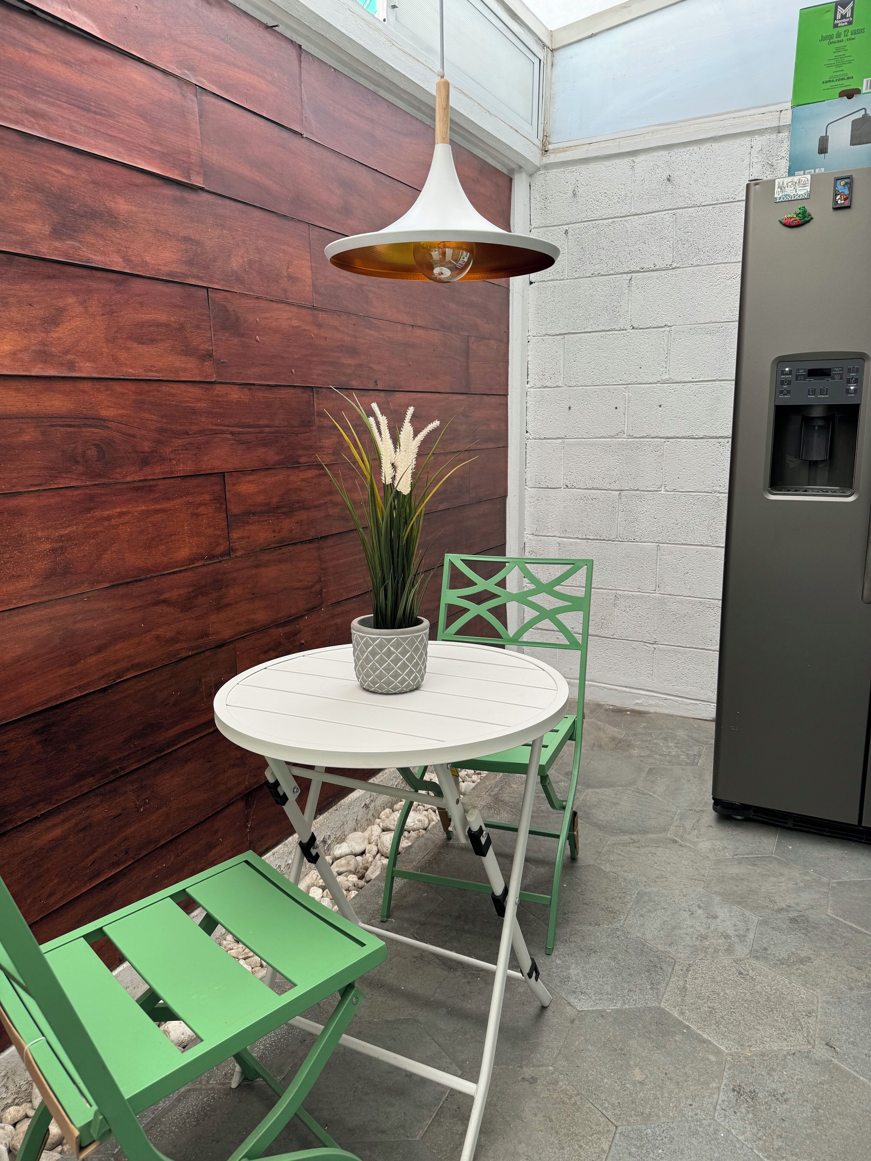 A small patio area with a round table, a potted plant, and a green chair.