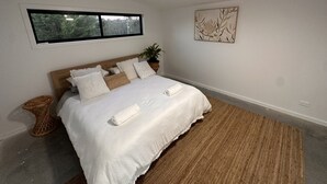 A modern bedroom with a large bed, a ceiling fan, a window with a view of trees, and a decorative wall piece.