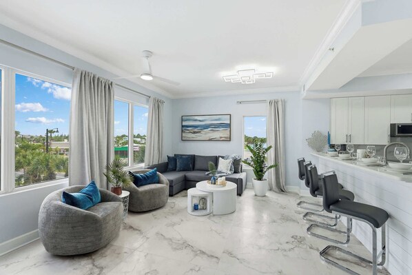 Una sala de estar moderna con un sofá, sillones, una mesa de centro y un comedor con sillas y una barra.