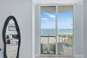 A room with a large mirror, a view of the ocean, and a balcony with chairs.