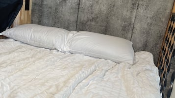 Een bed met een witte quilt en kussens, tegen een betonnen hoofdeinde, in een kamer met houten wanden.