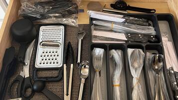 Een lade gevuld met verschillende keukenaccessoires en keukengereedschap, waaronder een rasp, schaar en een set lepels.