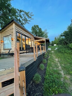 Una cabaña de madera con terraza, mobiliario exterior y un área cubierta con luces colgantes.