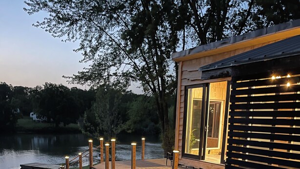 A wooden deck leading to a cabin with a glass door, overlooking a lake.