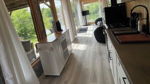 A modern kitchen with wooden flooring, white cabinets, and a large window offering a view of greenery.