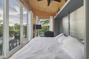 A bedroom with a large bed, a television, and a view of the outdoors through a sliding glass door.