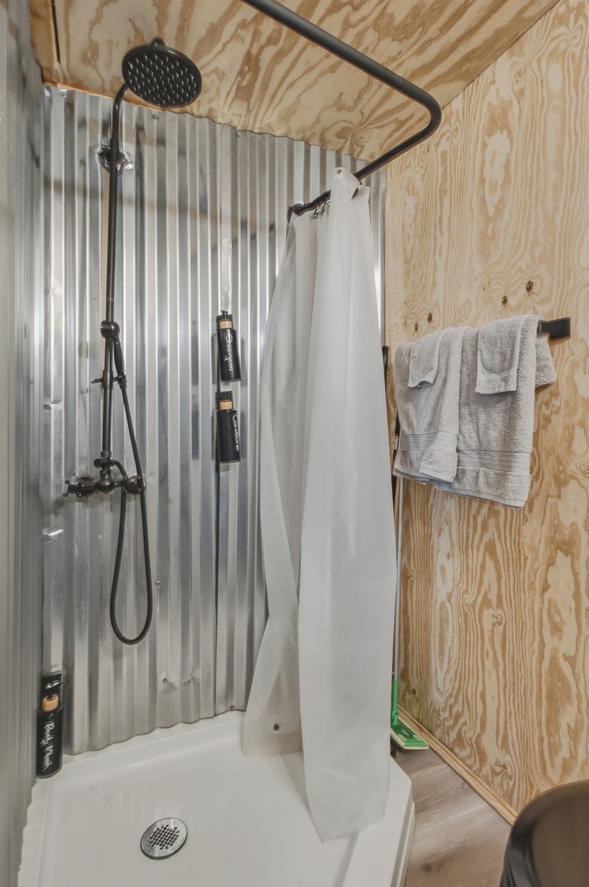 A shower with a handheld showerhead, a white curtain, and a towel rack with towels.