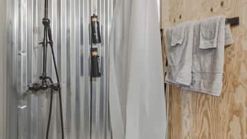 A shower with a handheld showerhead, a white curtain, and a towel rack with towels.