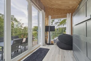 Una sala de estar moderna con un ventanal, un sillón orejero negro, una lámpara de pie y vistas a un jardín y un lago.