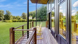 A wooden deck with a railing, a wooden pergola, and a view of a green landscape.
