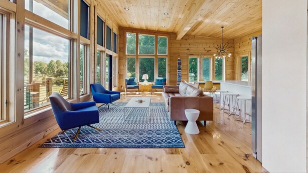 A spacious living room with large windows, wooden floors, and modern furniture.