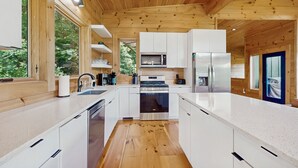 A modern kitchen with wooden walls, white cabinets, stainless steel appliances, and a central island.