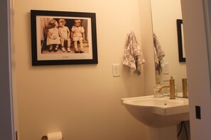 Een badkamer met een ingelijste foto aan de muur, een wastafel met kraan, en een handdoek aan de wand.