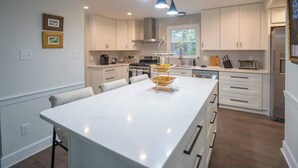A modern kitchen with white cabinets, a central island, and pendant lighting. - Fire pit - 6 Min to North Hills - Screened Porch (Raleigh)