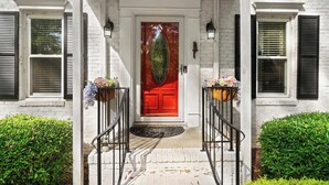 A white brick building with a red door, black shutters, and a white porch with a black railing. - Fire pit - 6 Min to North Hills - Screened Porch (Raleigh)