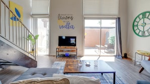 A modern living room with a flat-screen TV on a wooden stand, a sofa, a coffee table, and a large window with blinds. - Vintage Stay, 1BR Old Town Scottsdale Retreat (Scottsdale)