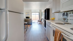 A modern kitchen with white appliances, a dining area with a sofa and chairs, and a view of the outdoors through a large window. - Vintage Stay, 1BR Old Town Scottsdale Retreat (Scottsdale)