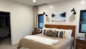 A bedroom with a bed, a nightstand, a window with curtains, a wall-mounted lamp, and a painting. - Parkside Paradise near Montana State University (Bozeman)
