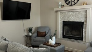 Un salon doté d’un téléviseur à écran plat, de canapés gris, d’une cheminée et d’une horloge décorative.