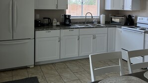 Une cuisine avec des meubles blancs, un évier, une cuisinière et un coin repas comprenant une table et des chaises.