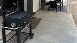 Une terrasse extérieure avec un barbecue, une table et des chaises, ainsi qu’un espace abrité.