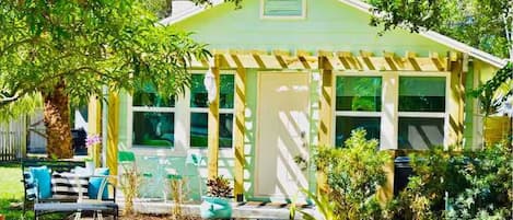 A small, single-story house with a front porch, a garage, and a garden area with plants and outdoor furniture.