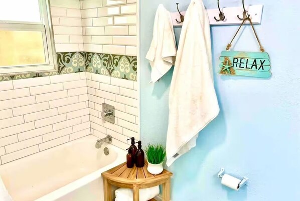 A bathroom with a bathtub, a wooden stool with toiletries, a towel rack, and a 'RELAX' sign. - Charming 3-bedroom cottage in Lake Worth Beach w. Enclosed Backyard & BBQ! (Lake Worth Beach)