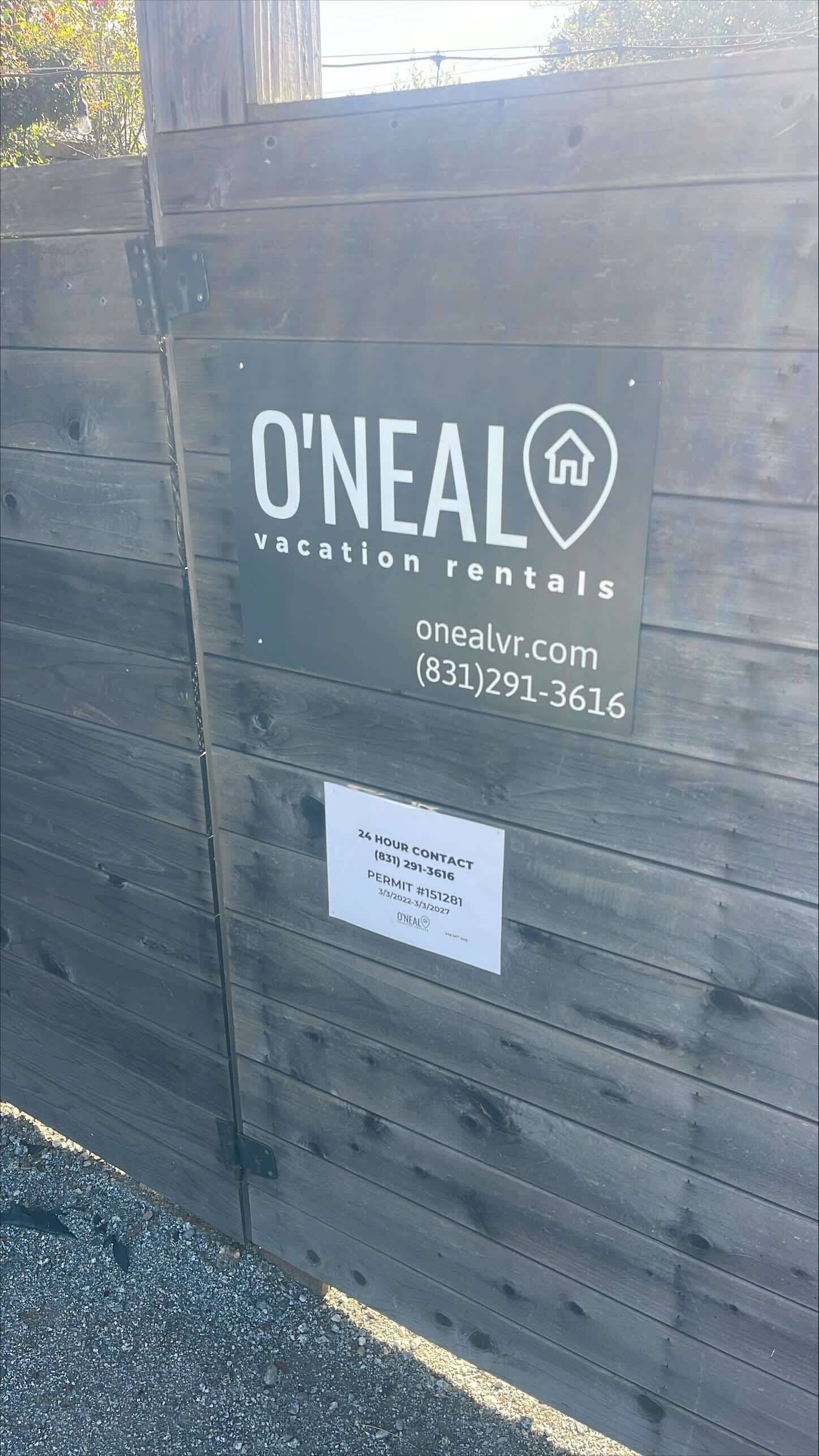 Puinen aita, jossa on kyltti, jossa lukee O'Neal Vacation Rentals, ja jossa on myös verkkosivuston osoite ja puhelinnumero.