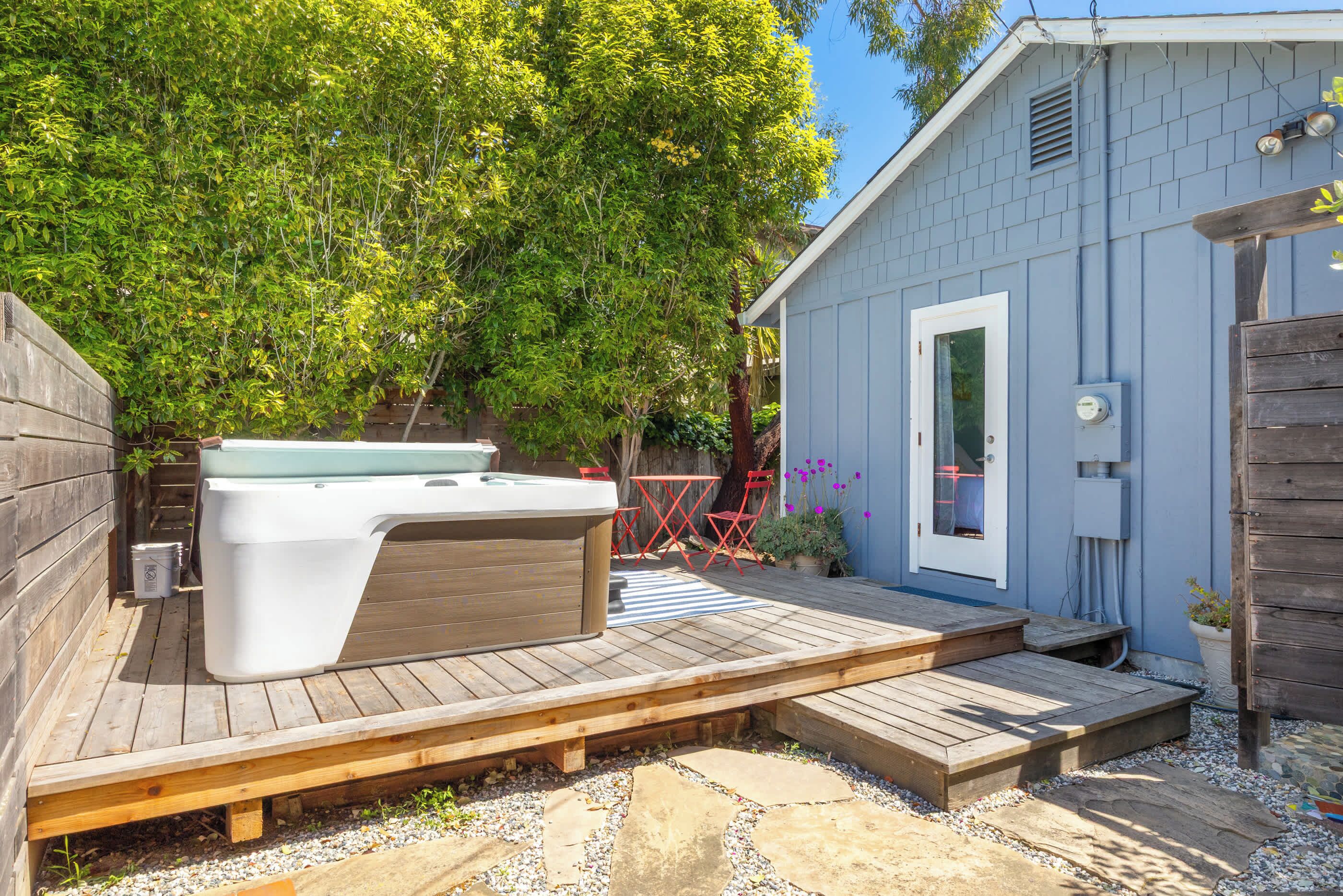 A wooden deck with a hot tub, a small shed, and a tree in the background.