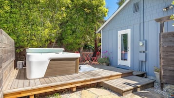 A wooden deck with a hot tub, a small shed, and a tree in the background.