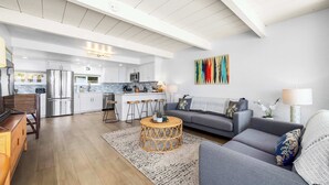 A spacious living area with a grey sofa, a coffee table, and a kitchen in the background.
