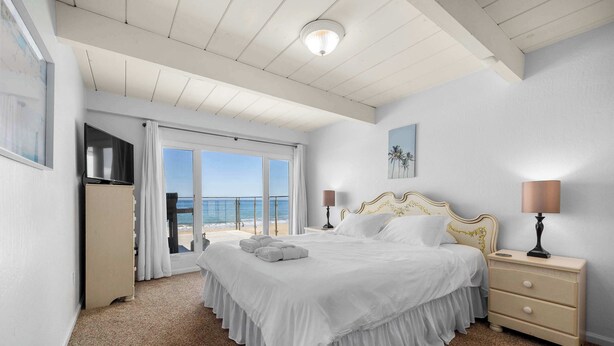 A hotel room with a large bed, a nightstand, a lamp, a painting, and a view of the sea.