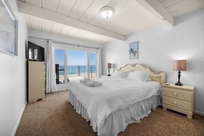 A hotel room with a large bed, a nightstand, a lamp, a painting, and a view of the sea.