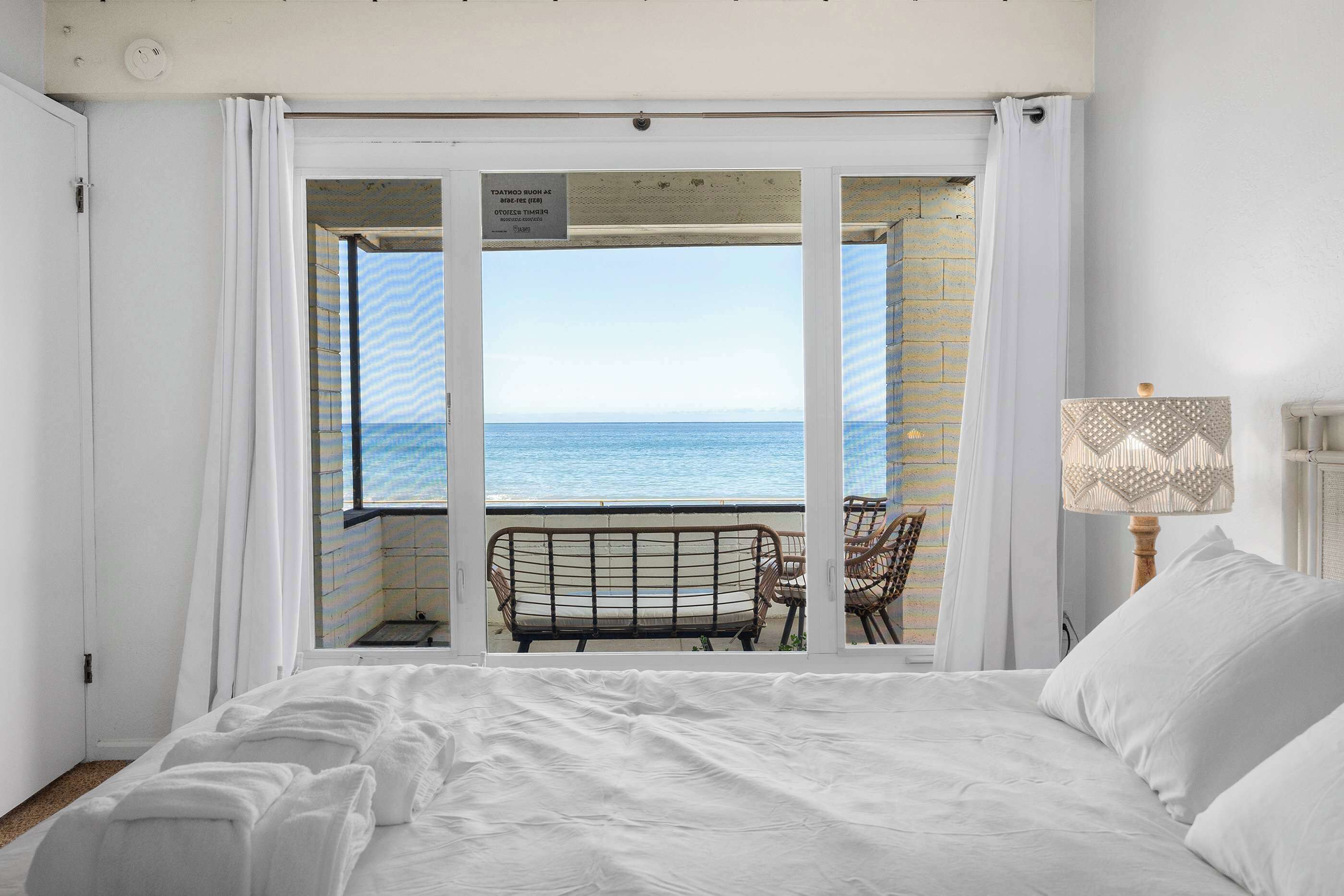 A bedroom with a large bed, a view of the sea through an open door, and a chair outside.