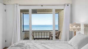 A bedroom with a large bed, a view of the sea through an open door, and a chair outside.