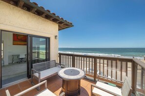 A balcony with a view of the ocean, a table, and a bench.