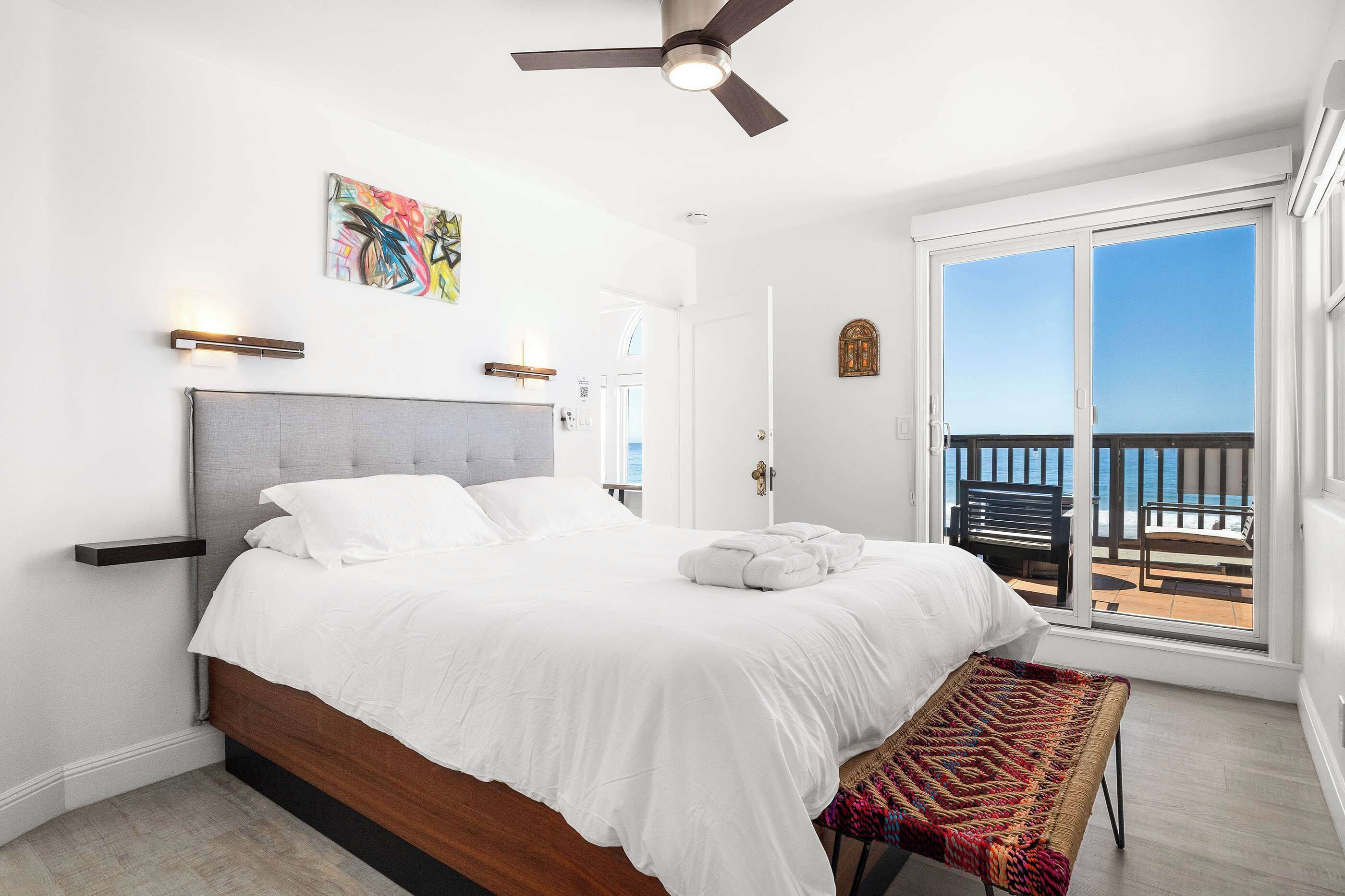Une chambre à coucher avec un lit, un ventilateur de plafond, une fenêtre donnant sur un beau paysage et une porte.