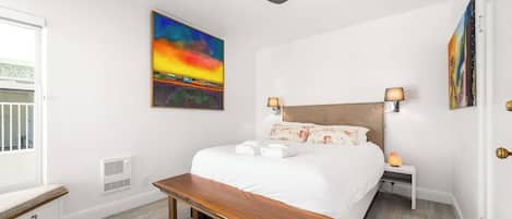 A bedroom with a bed, bedside lamps, a ceiling fan, a bench, and artwork on the walls.