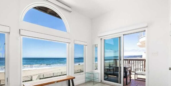 A room with large windows overlooking a beach, a glass door leading to an outdoor area with a table and chairs. - 3 Bedroom Rio Del Mar Home - Steps to Beach! (Aptos)